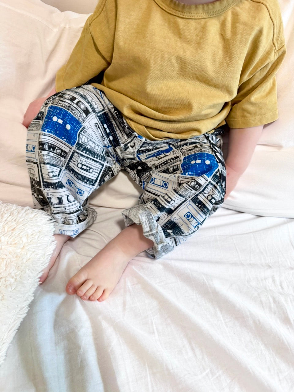 baby sitting on a bed in blue, black and white patterned pants