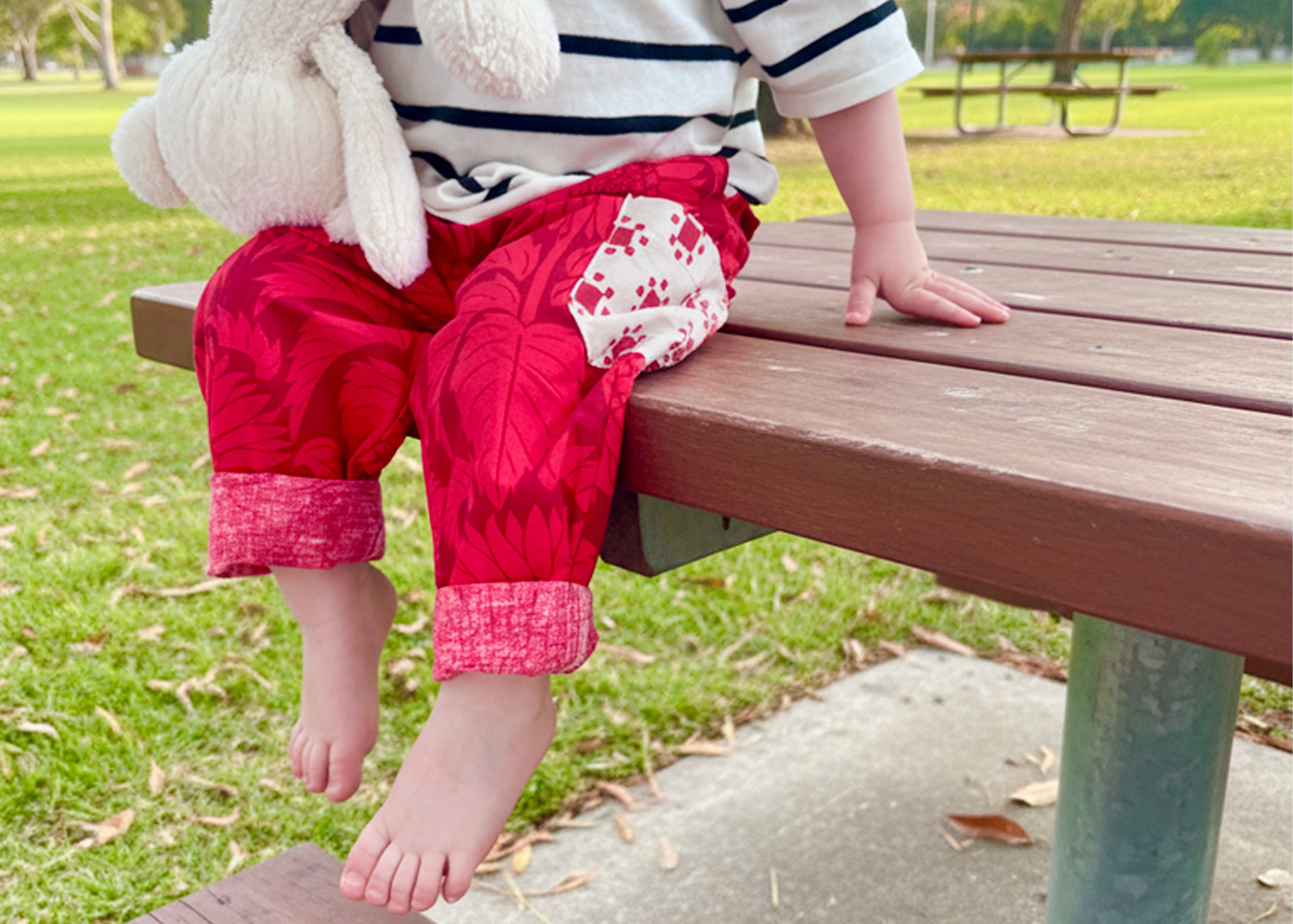 Child sitting on a bench in a park holding a stuffed bear toy.